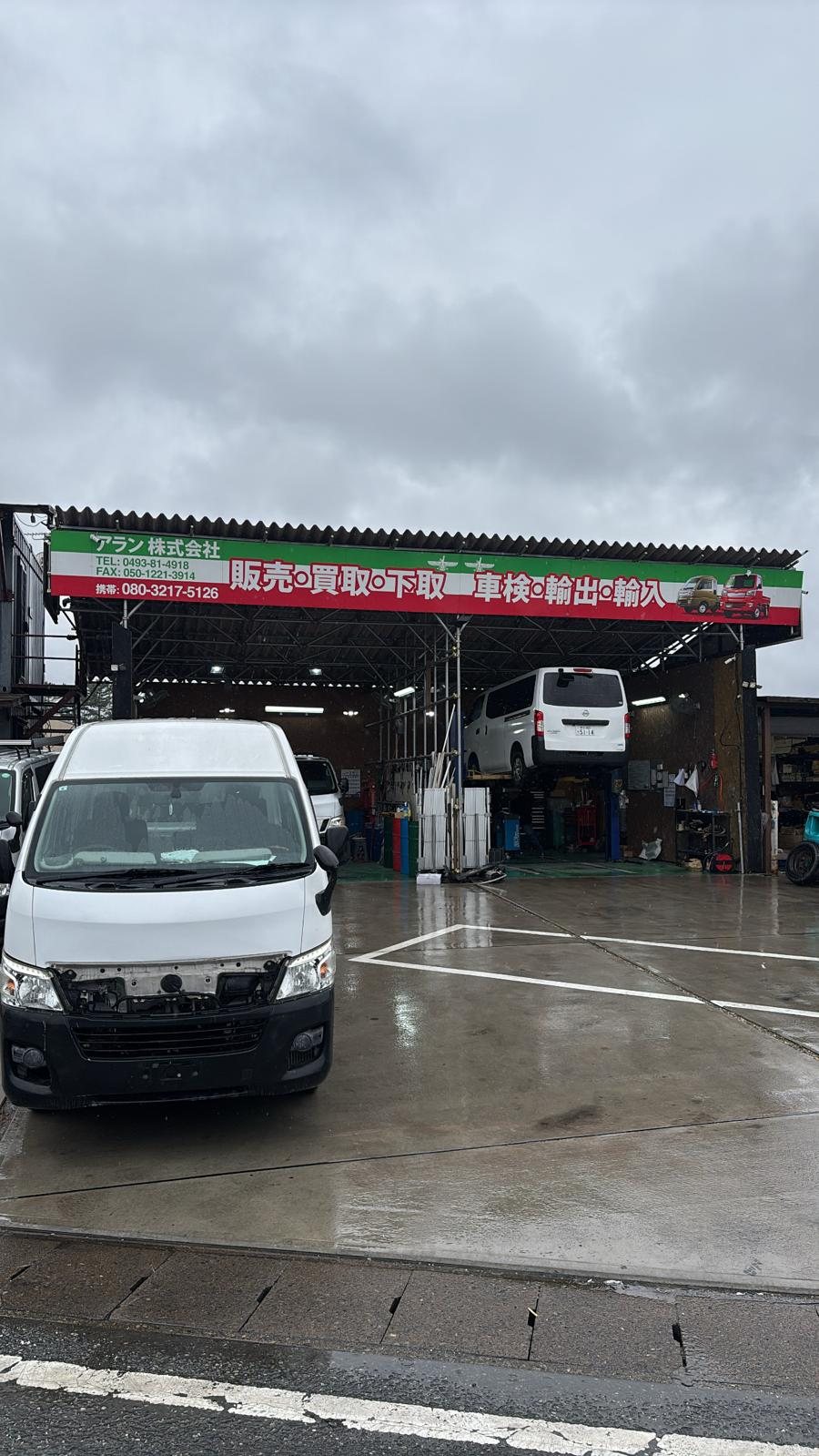 Außenansicht eines japanischen Partnerbetriebs für Fahrzeugaufbereitung bei Regen, davor ein weißer Transporter.
