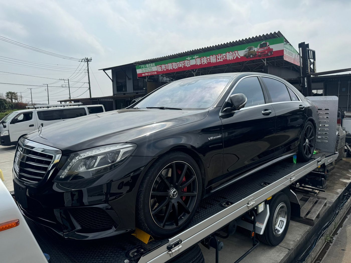 Eine schwarze Mercedes-AMG S-Klasse steht auf einem Flachbett-Transporter vor einem japanischen Betrieb.